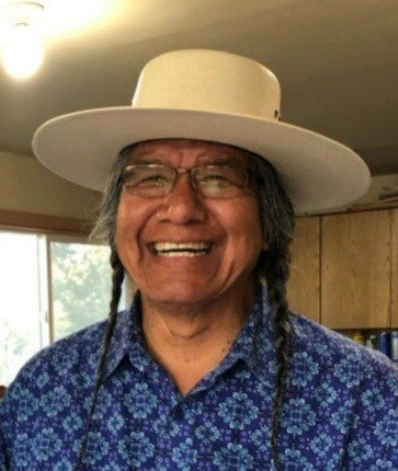 Wewa stands indoors with a tan brimmed hat and a blue patterned shirt