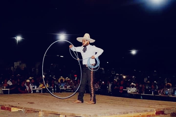 Josue Mendoza performing rope skills on a stage at night. He is wearing a white hat, white shirt, and black pants.