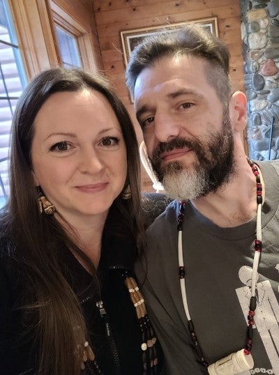 Beth Gipson standing next to a man with a beard and beaded necklace. 